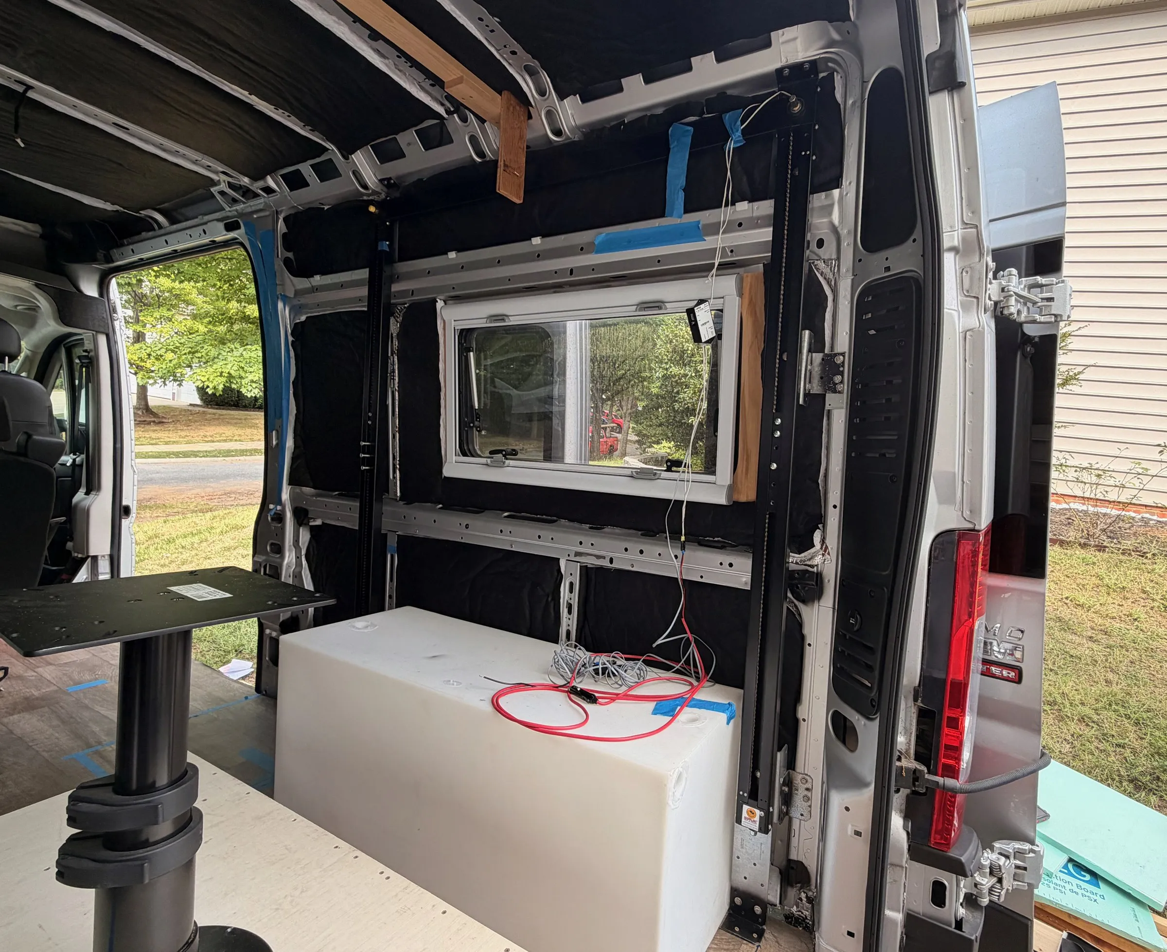 Passenger-side rear wall with an installed window, insulation, bed-lift track and a white water tank on the floor