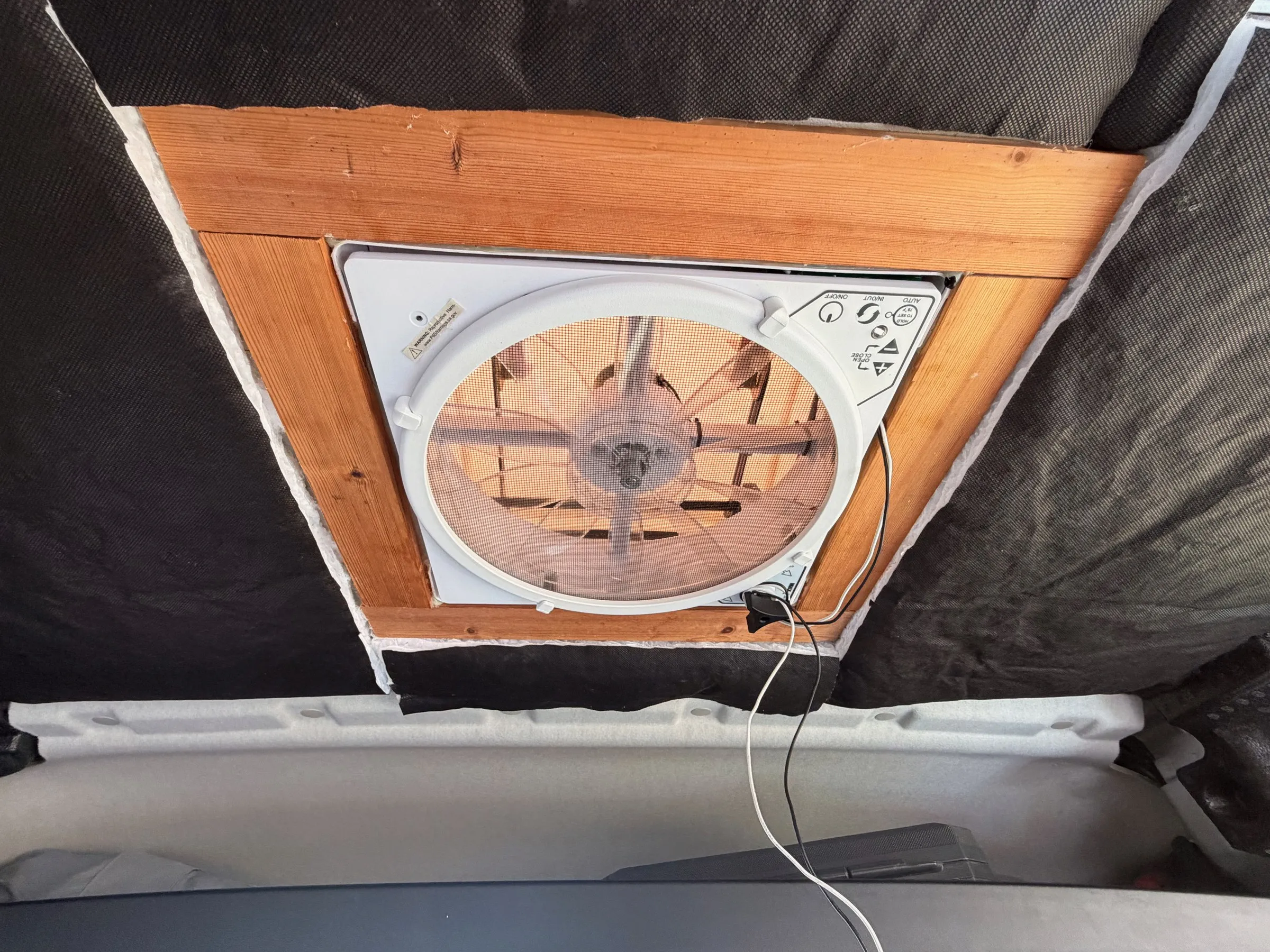 Roof vent fan from inside, framed in wood within black ceiling insulation